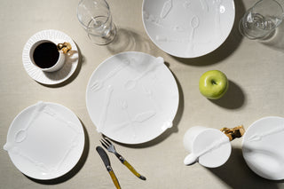 White ceramic plates with artistic designs on a neutral surface with a cup, glass, and apple.