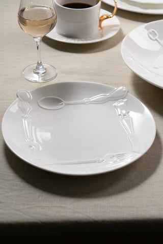 White ceramic plate with cutlery on a beige tablecloth, accompanied by a glass of white wine and a cup of coffee.
