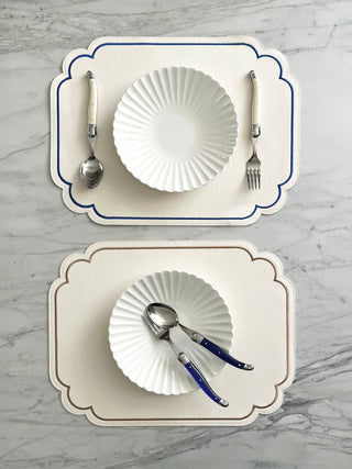 Two placemats with white dishes, silverware, and decorative elements on a marble surface.