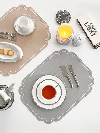 Table setting with plates, cutlery, and a candle on decorative placemats.