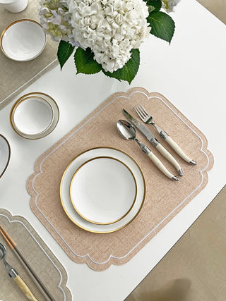 Table setting with white plates, silverware, and a vase of white flowers on a coral placemat.