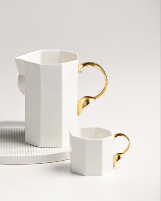 White ceramic pitcher and cup with gold accents on a light gray background