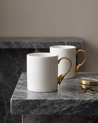 Two white mugs with gold handles on a dark marble surface.