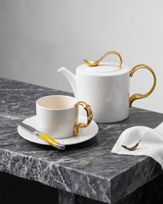 White teapot and cup with gold accents on a marble surface
