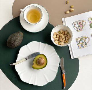 Tea cup, avocado, nuts, and knives on a green plate with a magazine in the background.